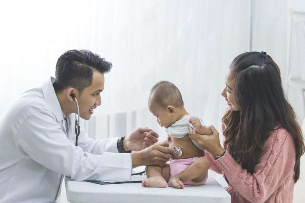 A pediatrician is checking a baby during their first appointment with a stethoscope.