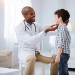 A pediatrician is conducting essential health checks on a young boy, specifically examining his ear for any potential issues.