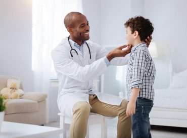 A pediatrician is conducting essential health checks on a young boy, specifically examining his ear for any potential issues.