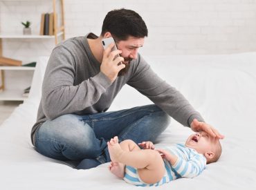 Un hombre hablando por teléfono mientras sostiene a un bebé en una cama.