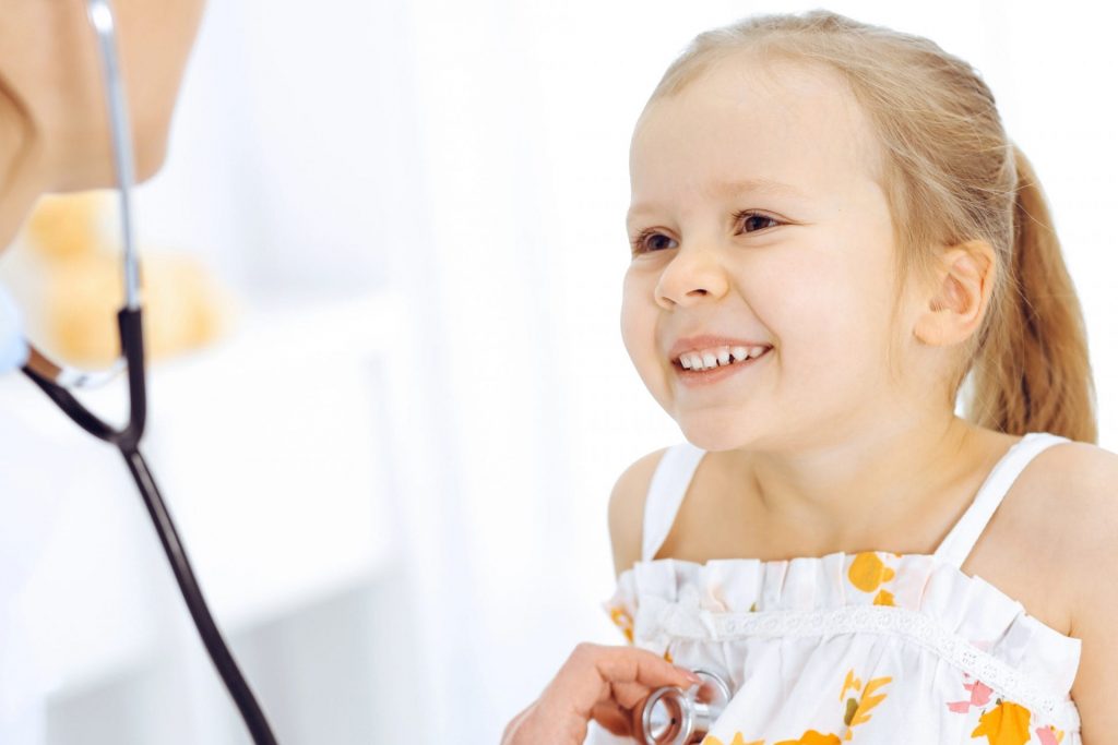 A key moment in a child's health journey is captured as a little girl smiles while a doctor discovers something through her stethoscope.