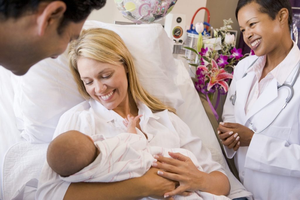 A woman is holding a baby in a hospital bed while receiving guidance from a good pediatrician.