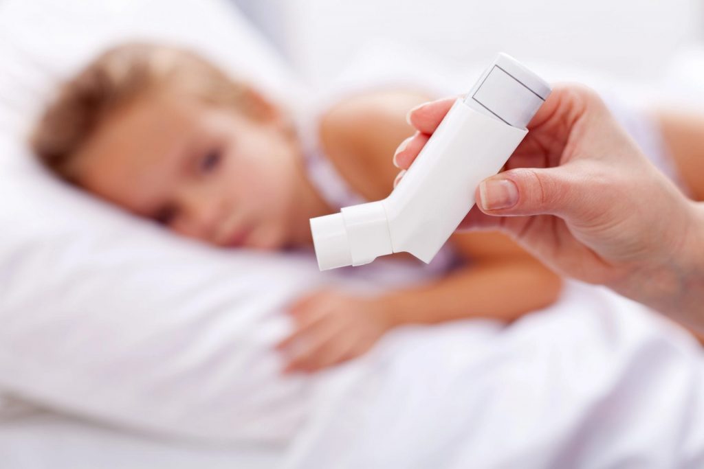 A child is effectively using an asthma inhaler in bed, benefiting from pediatrician-recommended asthma treatment.